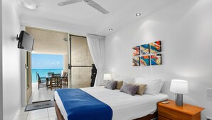 Una habitación de hotel con cama, mesita de noche, obras de arte y vista al océano.