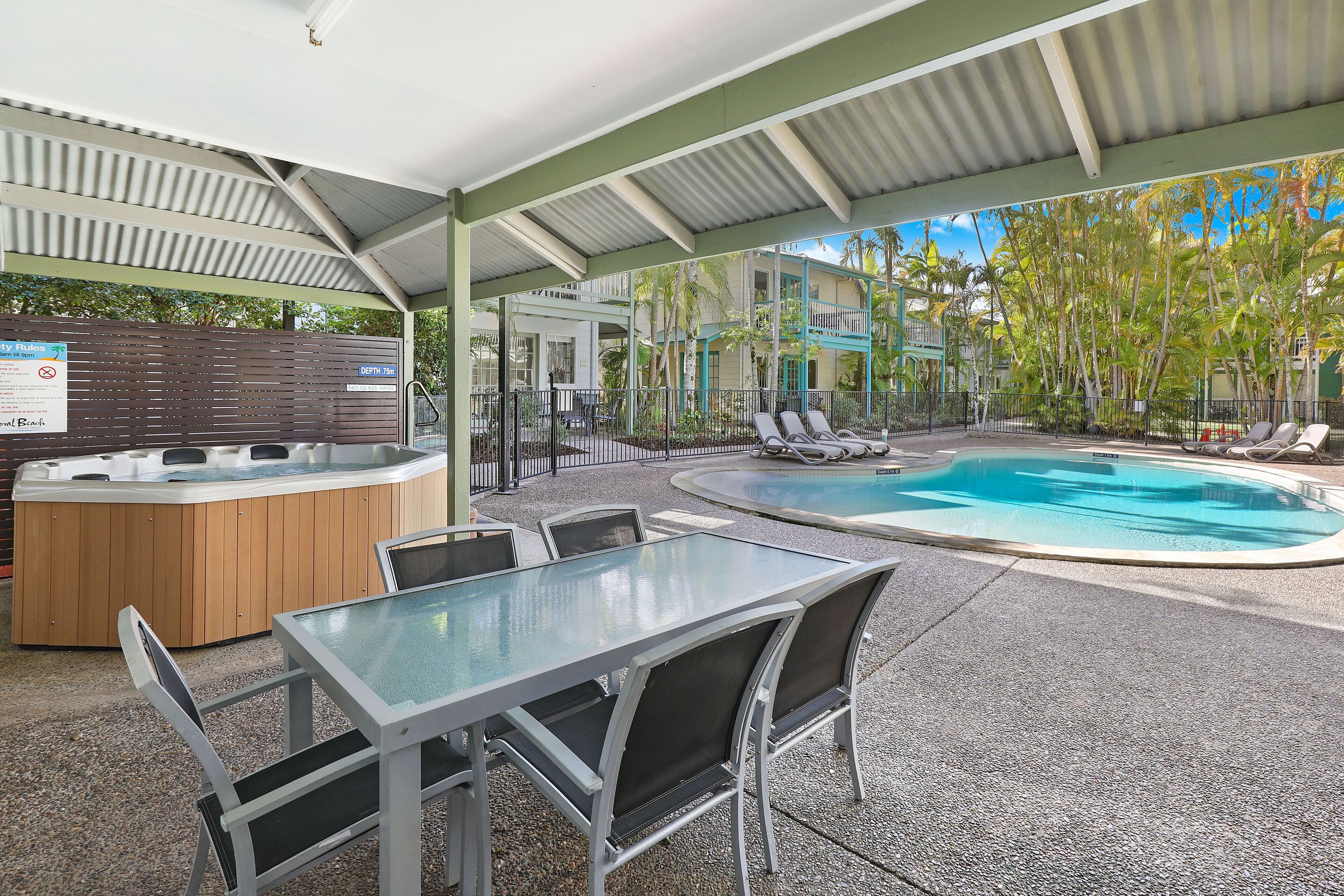 An outdoor pool area with a hot tub, lounge chairs, and a covered patio.