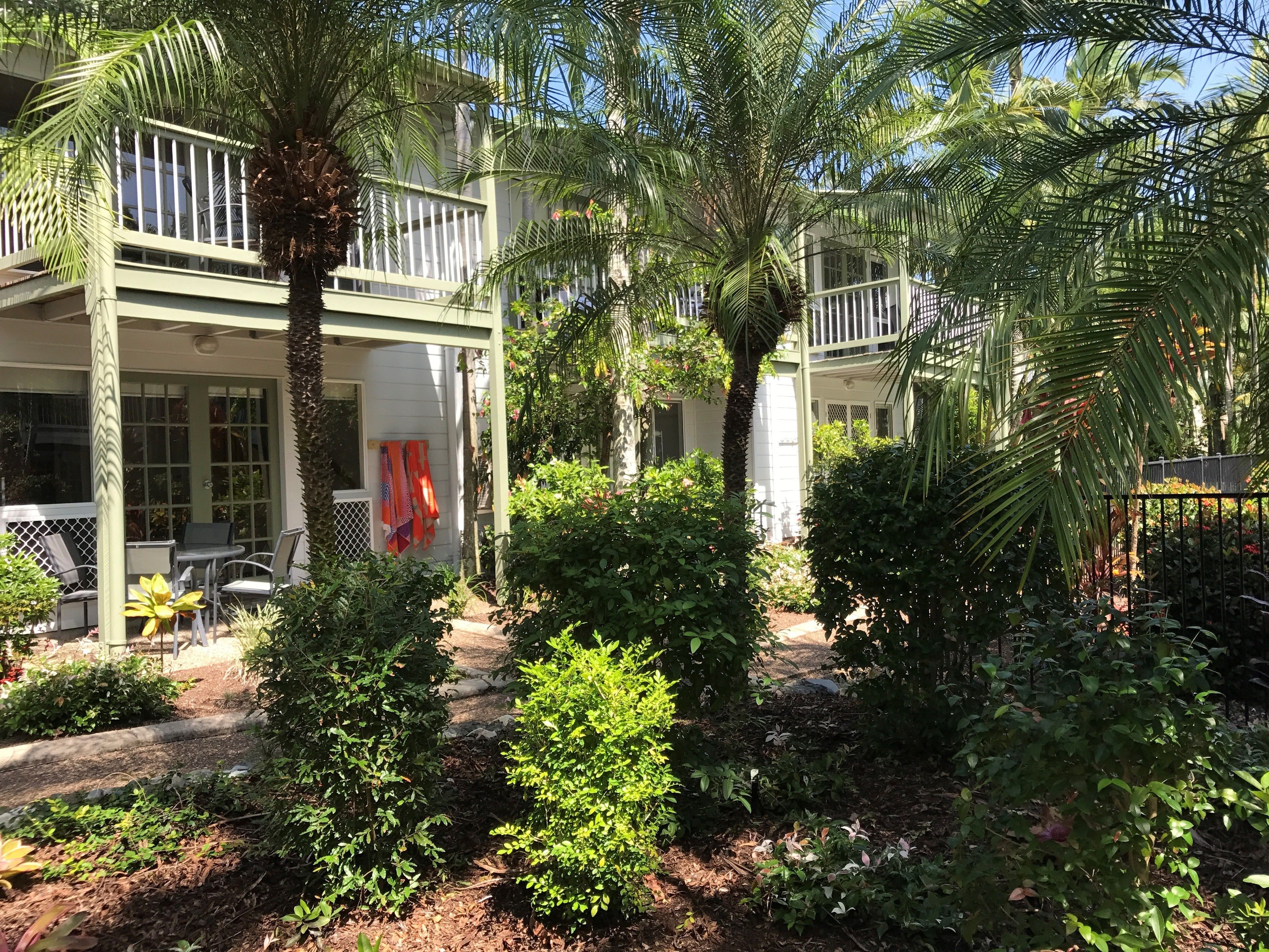 A two-story building with a covered patio area, outdoor seating, and lush greenery.