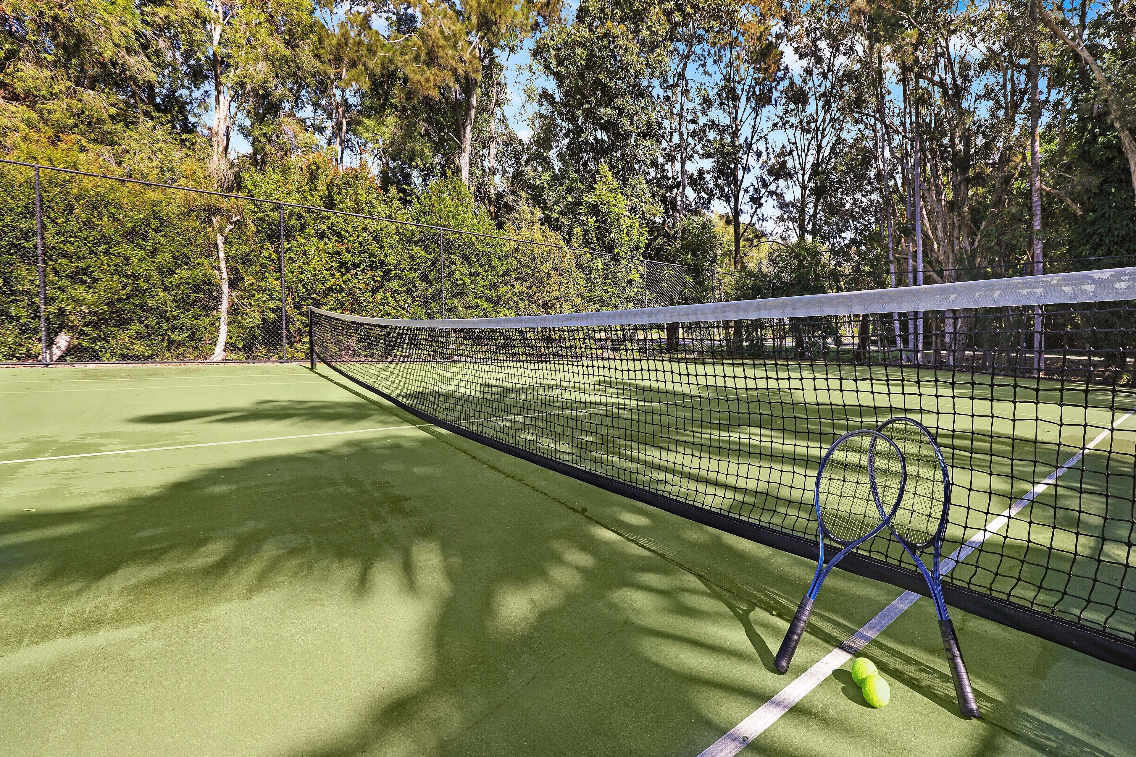 A tennis court with a net, two tennis rackets, and a tennis ball.