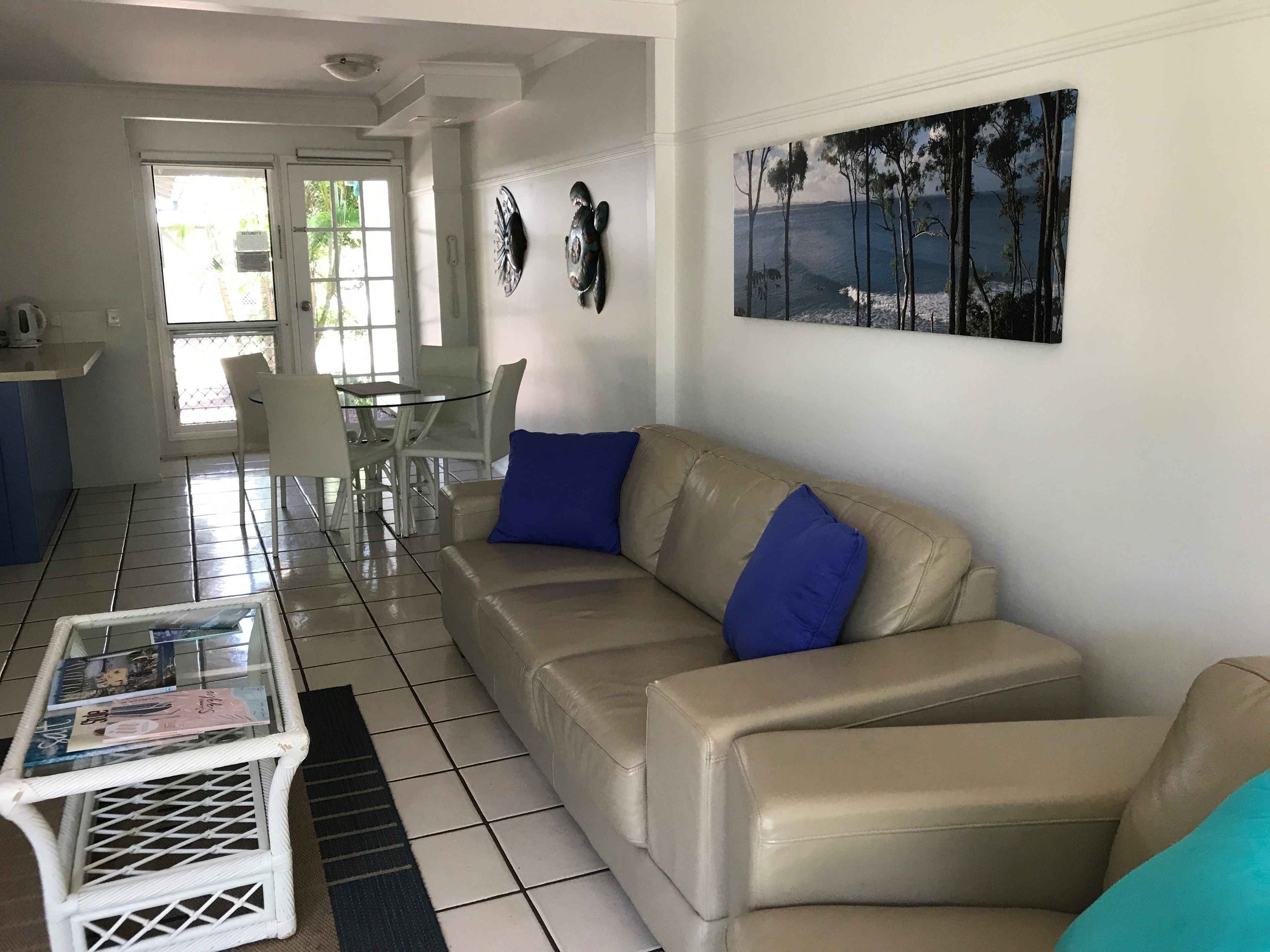 A living room with a beige leather sofa, a glass coffee table, and a dining area with a glass table and chairs.