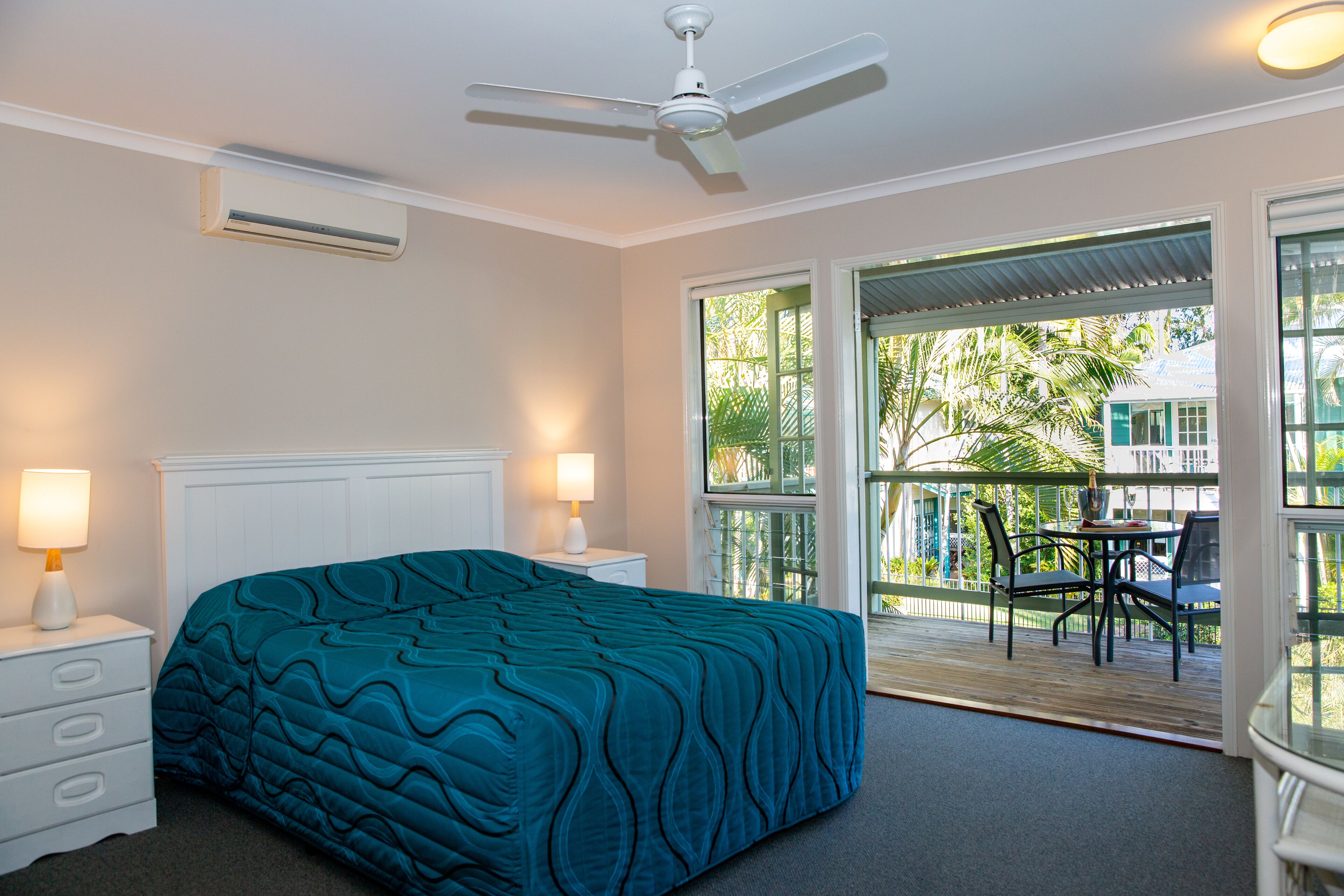 Un dormitorio con cama, lámparas de noche, ventilador de techo y vistas al exterior a través de una puerta corrediza de vidrio.