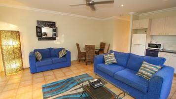 A living room with two blue sofas, a coffee table, and a dining area with wicker chairs.
