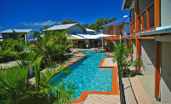 A swimming pool surrounded by palm trees and modern buildings with a clear blue sky.