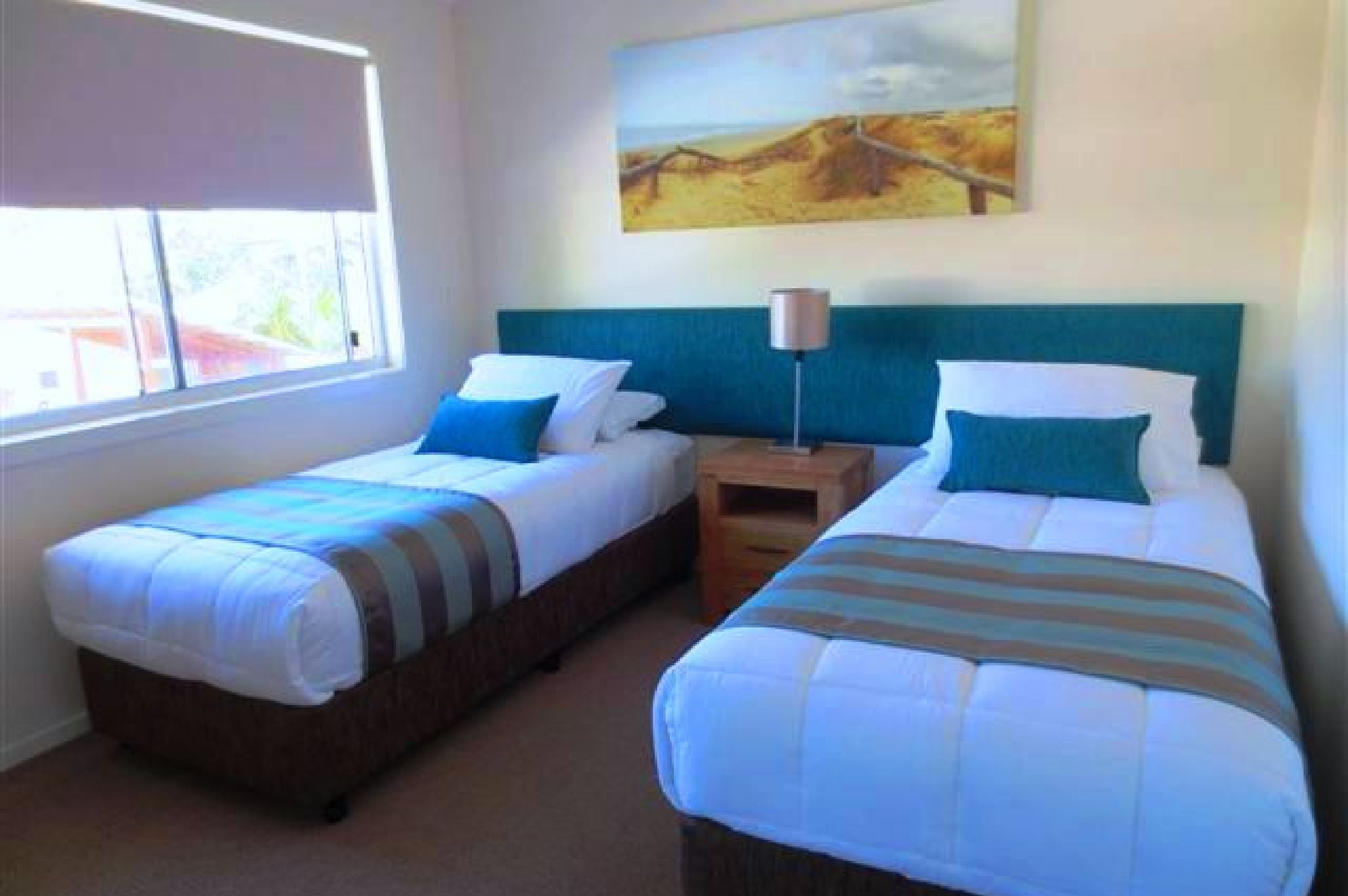 A room with two single beds, a nightstand, a lamp, and a painting on the wall.