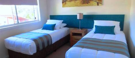 A room with two single beds, a nightstand, a lamp, and a painting on the wall.