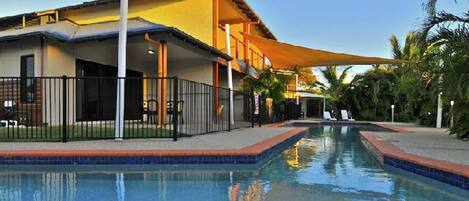 Un hotel con piscina, mobiliario exterior y un patio cubierto.