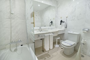 Features a glass-enclosed shower, standalone sink, and toilet with bidet attachment.
