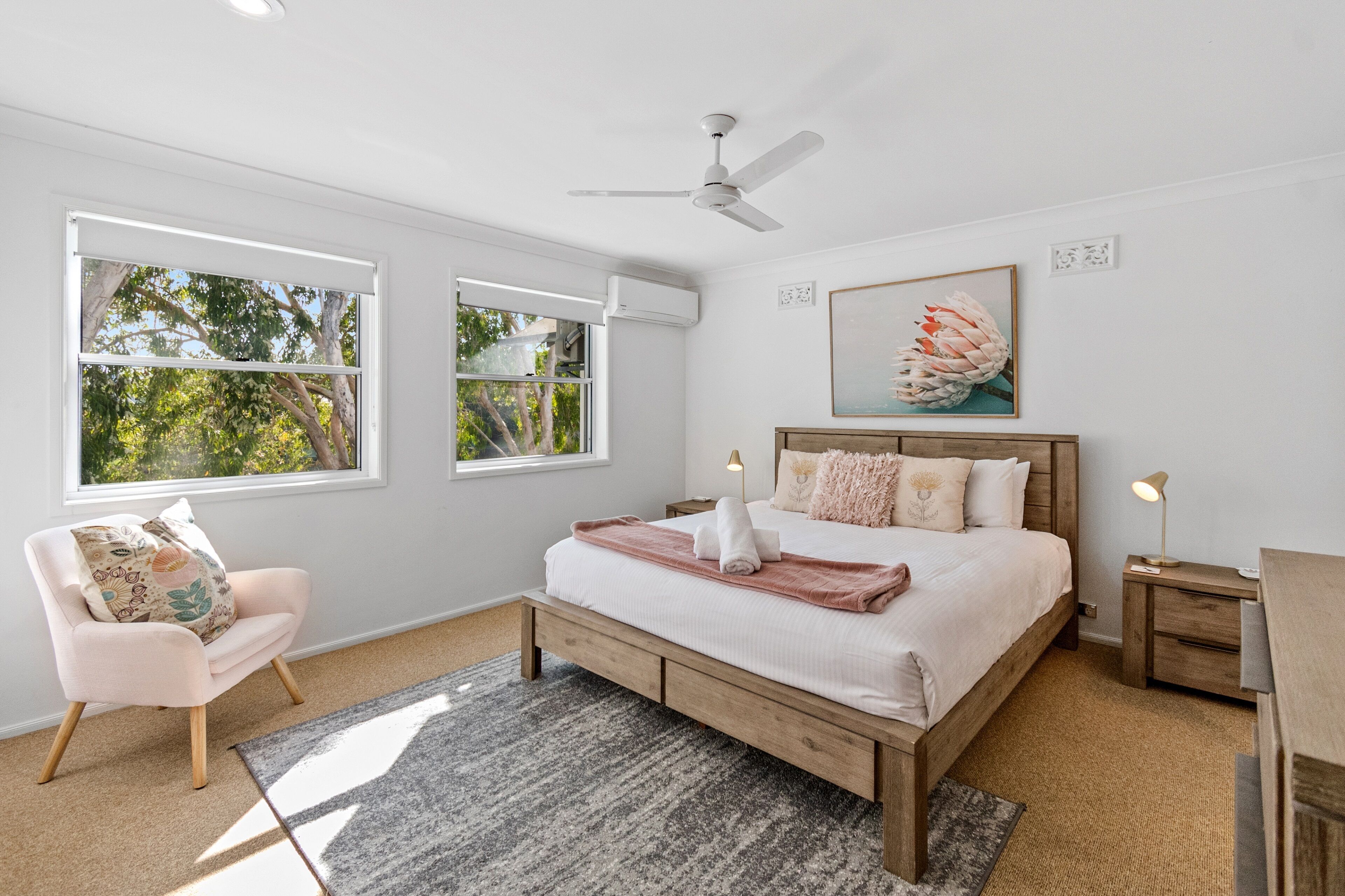 A bedroom with a bed, a chair, a ceiling fan, and a window.