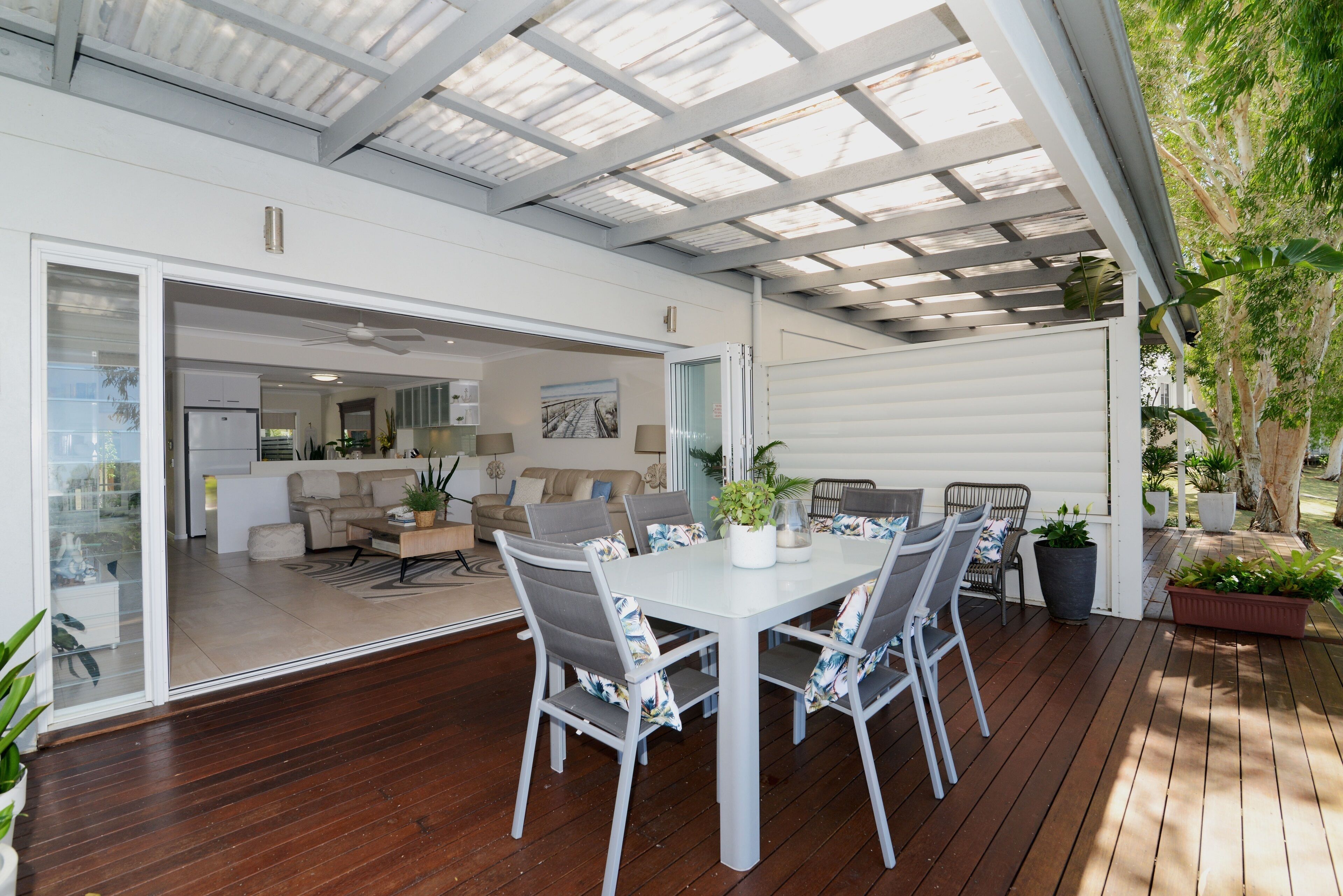 A covered patio with a dining table and chairs, a sofa, and a kitchen area visible through an open door.