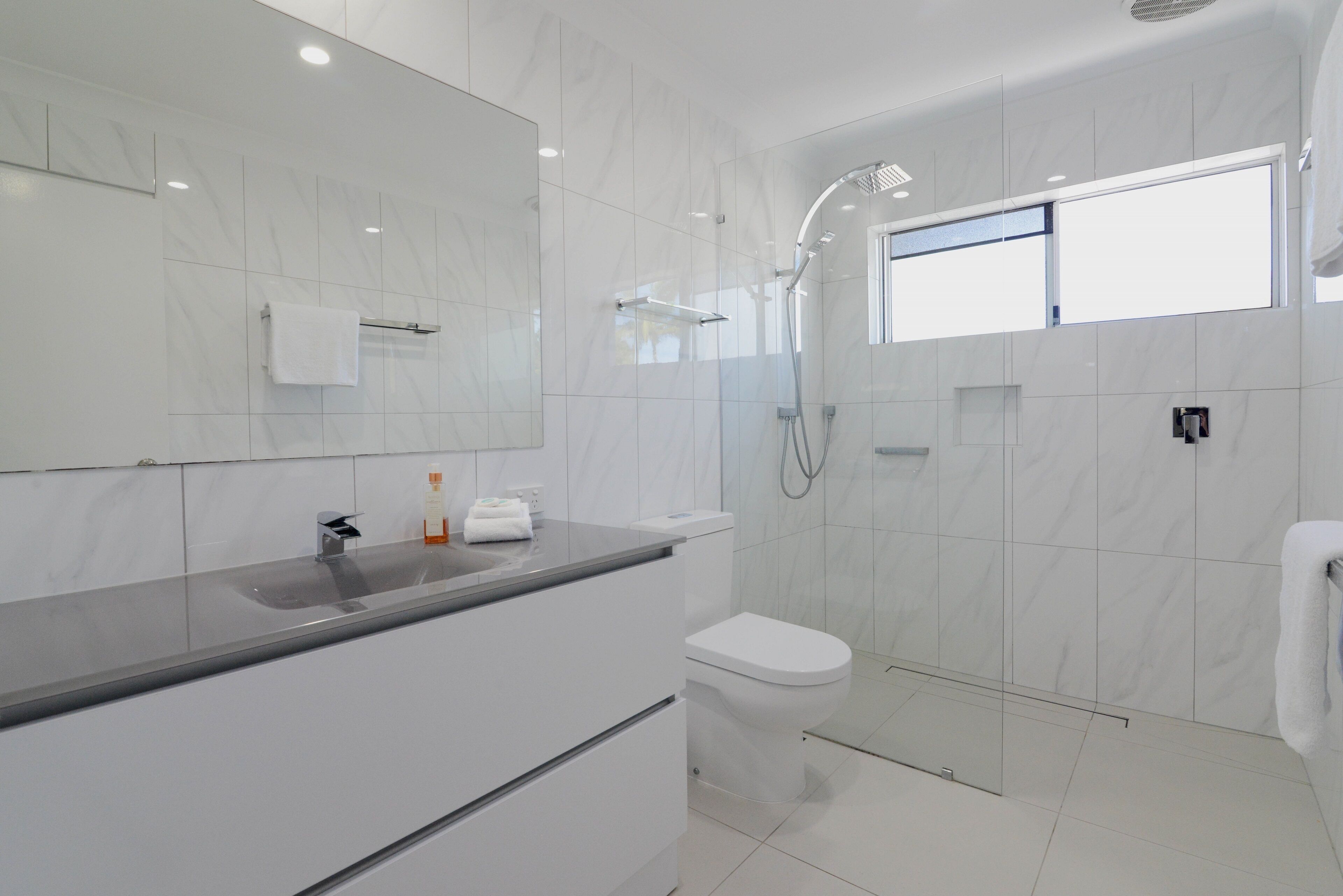 Une salle de bain moderne avec un grand miroir, un lavabo, des toilettes et une douche.