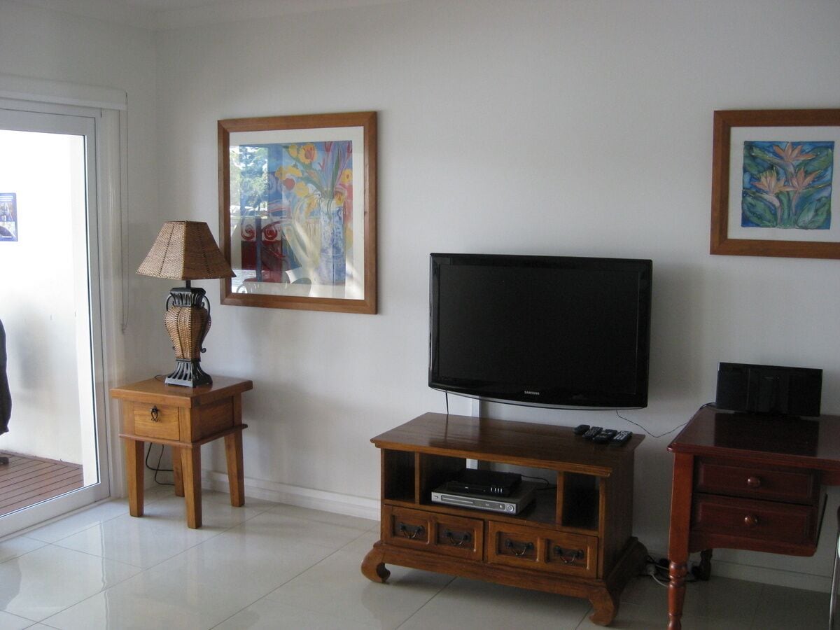 Een woonkamer met een flatscreen televisie, een houten tv-meubel en twee schilderijen aan de muur.