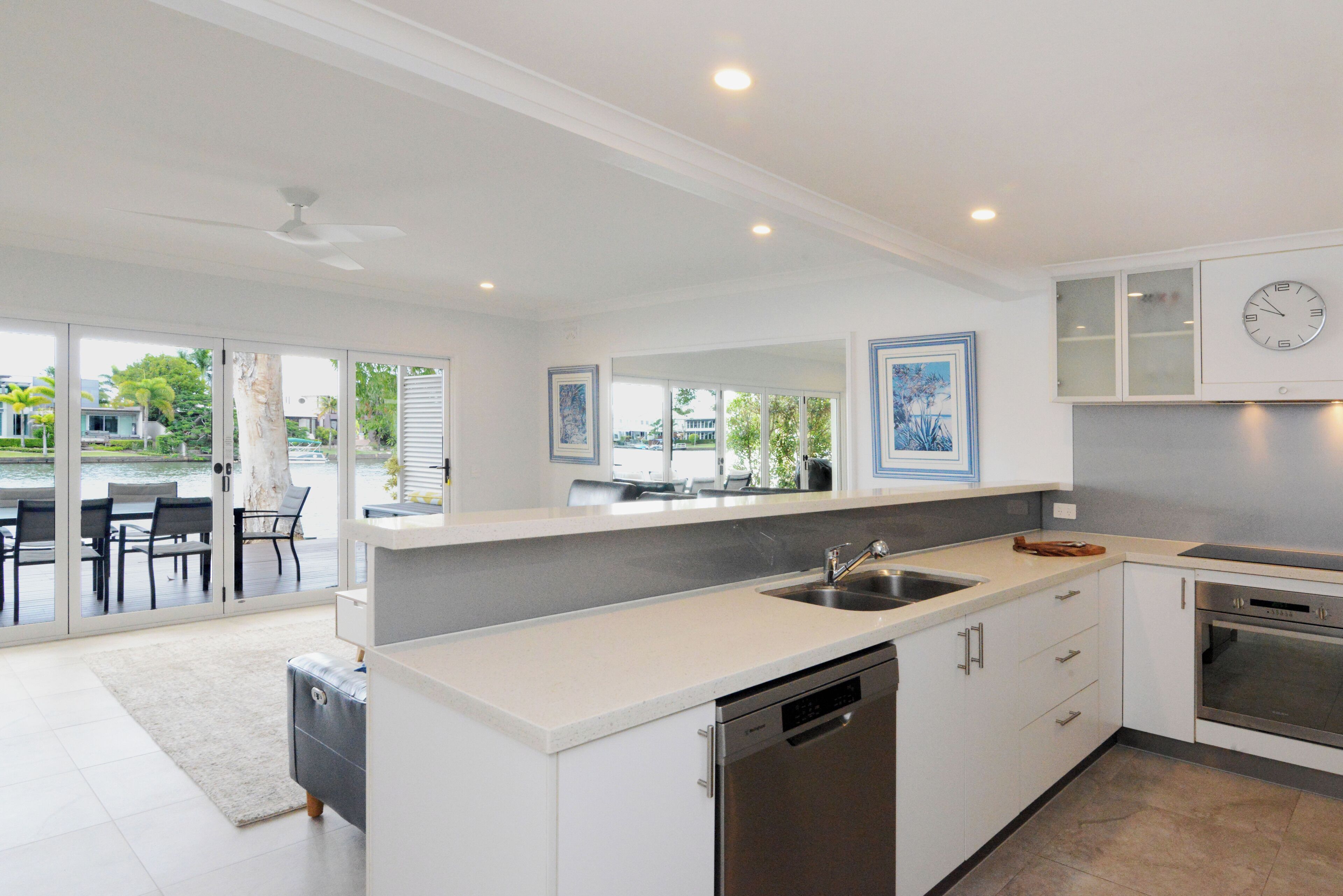 A modern kitchen with a dishwasher, oven, and a large window overlooking a patio area.
