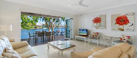 A spacious living room with a large window overlooking a pool, a ceiling fan, and a flat-screen TV on a wooden table.