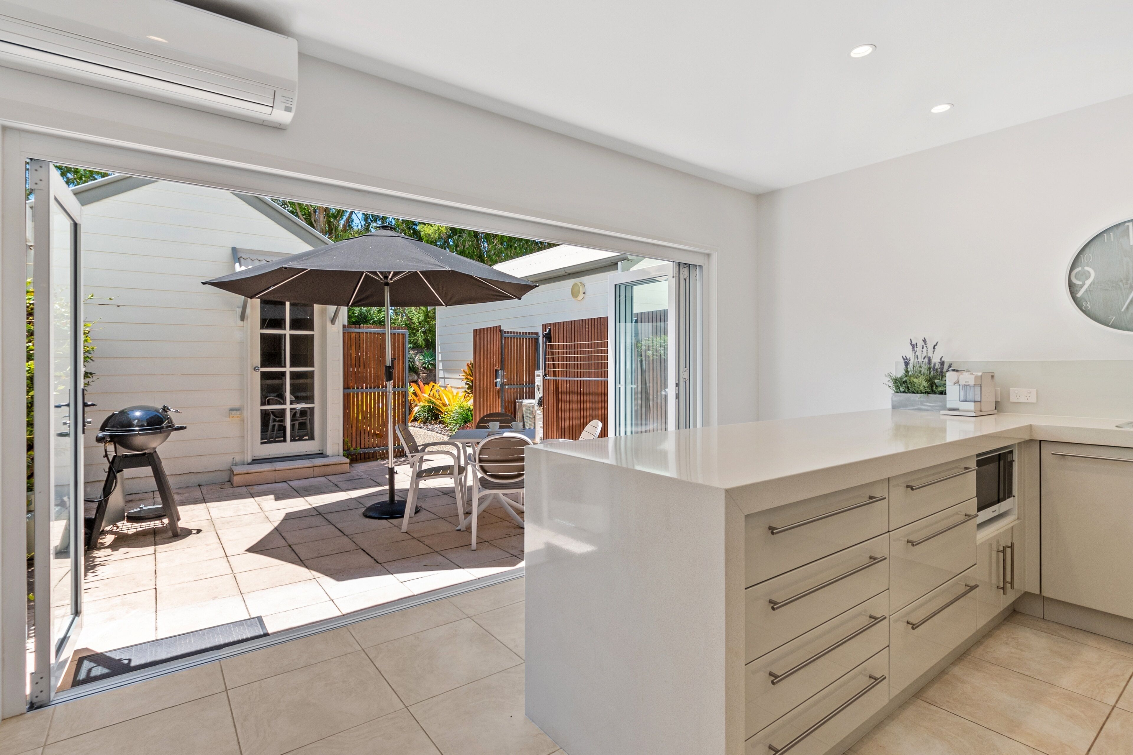 A modern kitchen with a large island, a dining area with outdoor seating, and a sliding glass door leading to a patio.