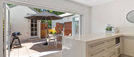 A modern kitchen with a large island, a dining area with outdoor seating, and a sliding glass door leading to a patio.
