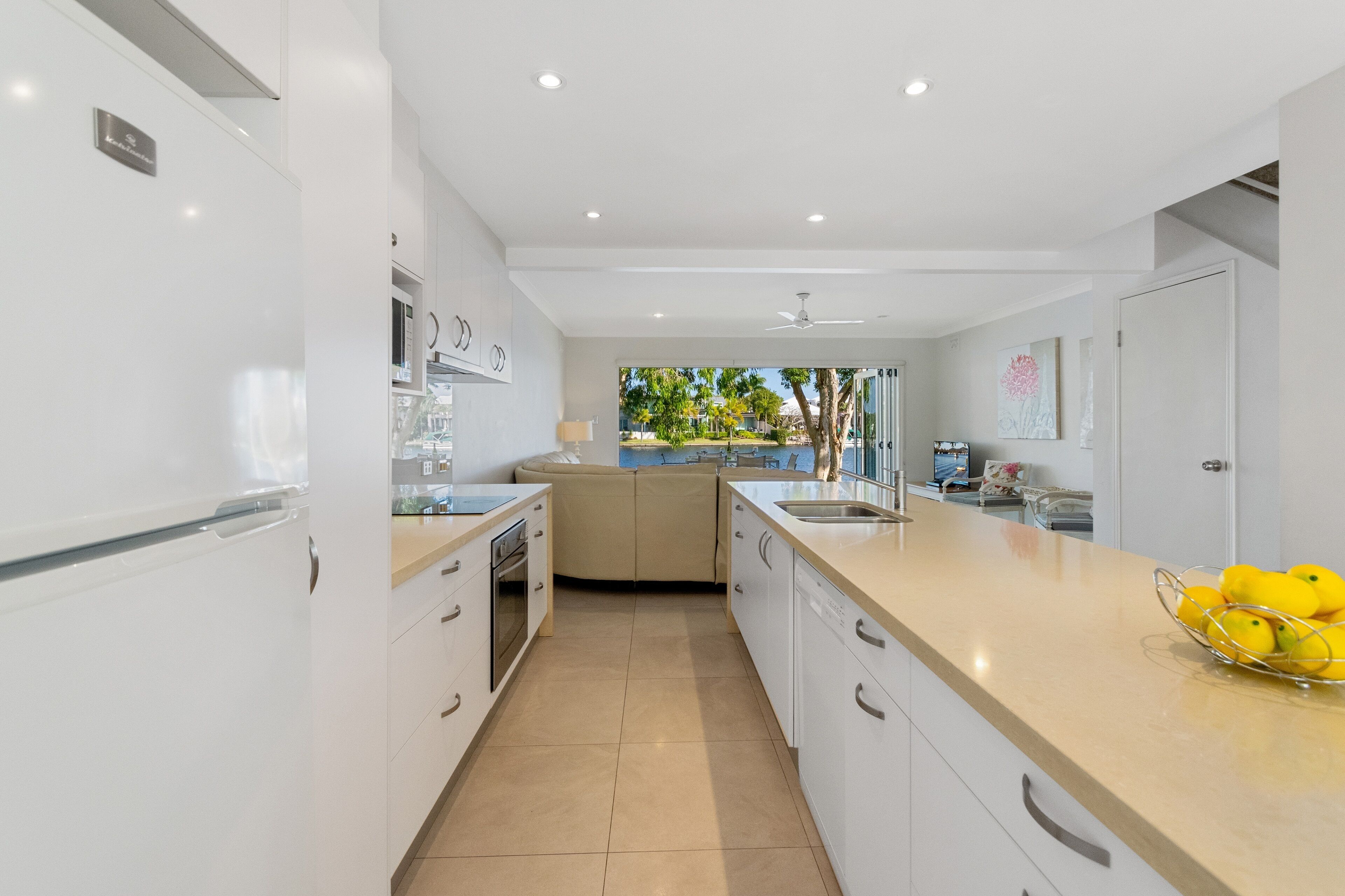 Une cuisine moderne avec des meubles blancs, un plan de travail beige et une vue sur un jardin.