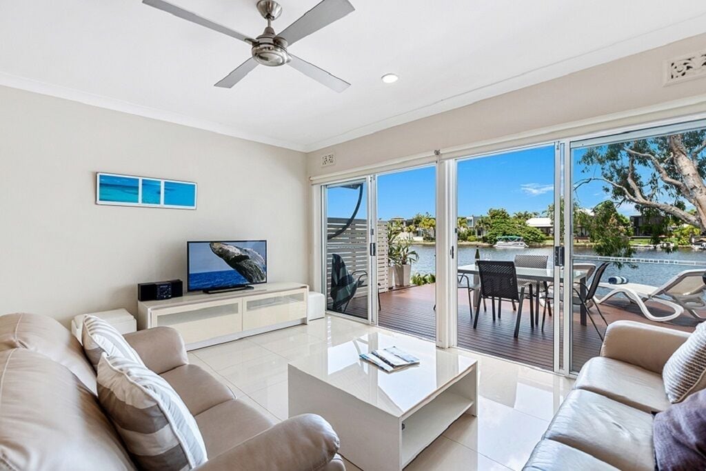 A modern living room with a flat-screen TV, a ceiling fan, and a view of a pool and greenery outside.