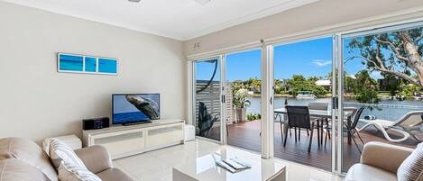 A modern living room with a flat-screen TV, a ceiling fan, and a view of a pool and greenery outside.
