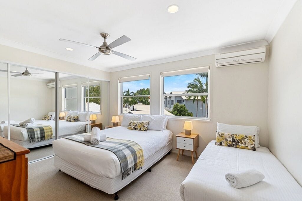 A hotel room with two beds, a ceiling fan, large windows, and an air conditioning unit.