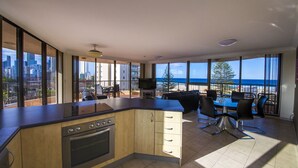 Et moderne køkken med en stor ø, spiseområde med stole og store vinduer med udsigt over byen.
