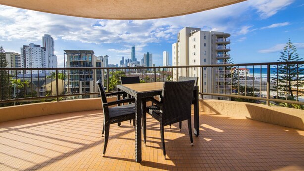 En balkon med et bord og stole, der ud til en byudsigt med høje bygninger og en klar himmel.