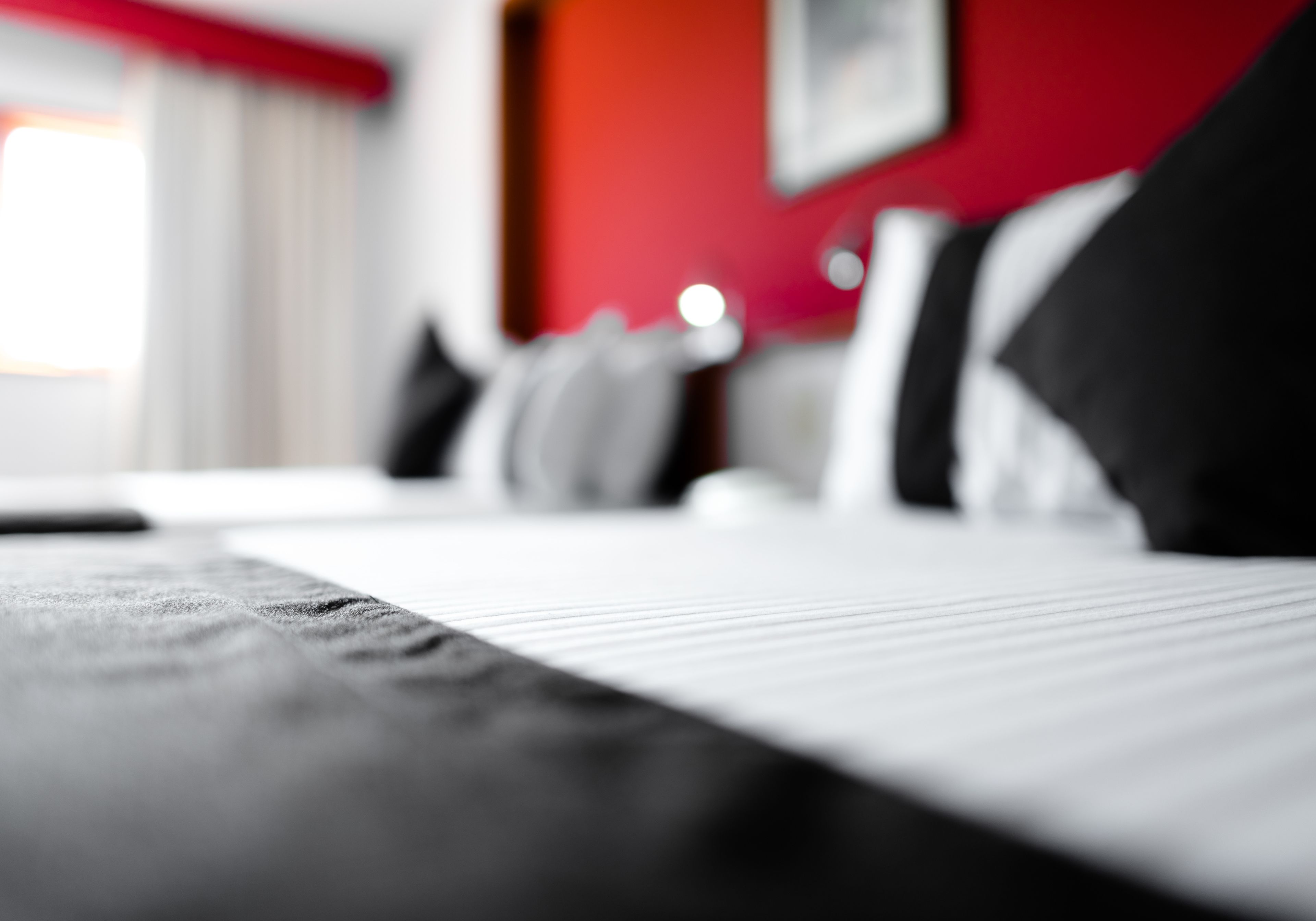 Primer plano de una cama con colcha a rayas, una pared roja y una ventana con cortinas al fondo.