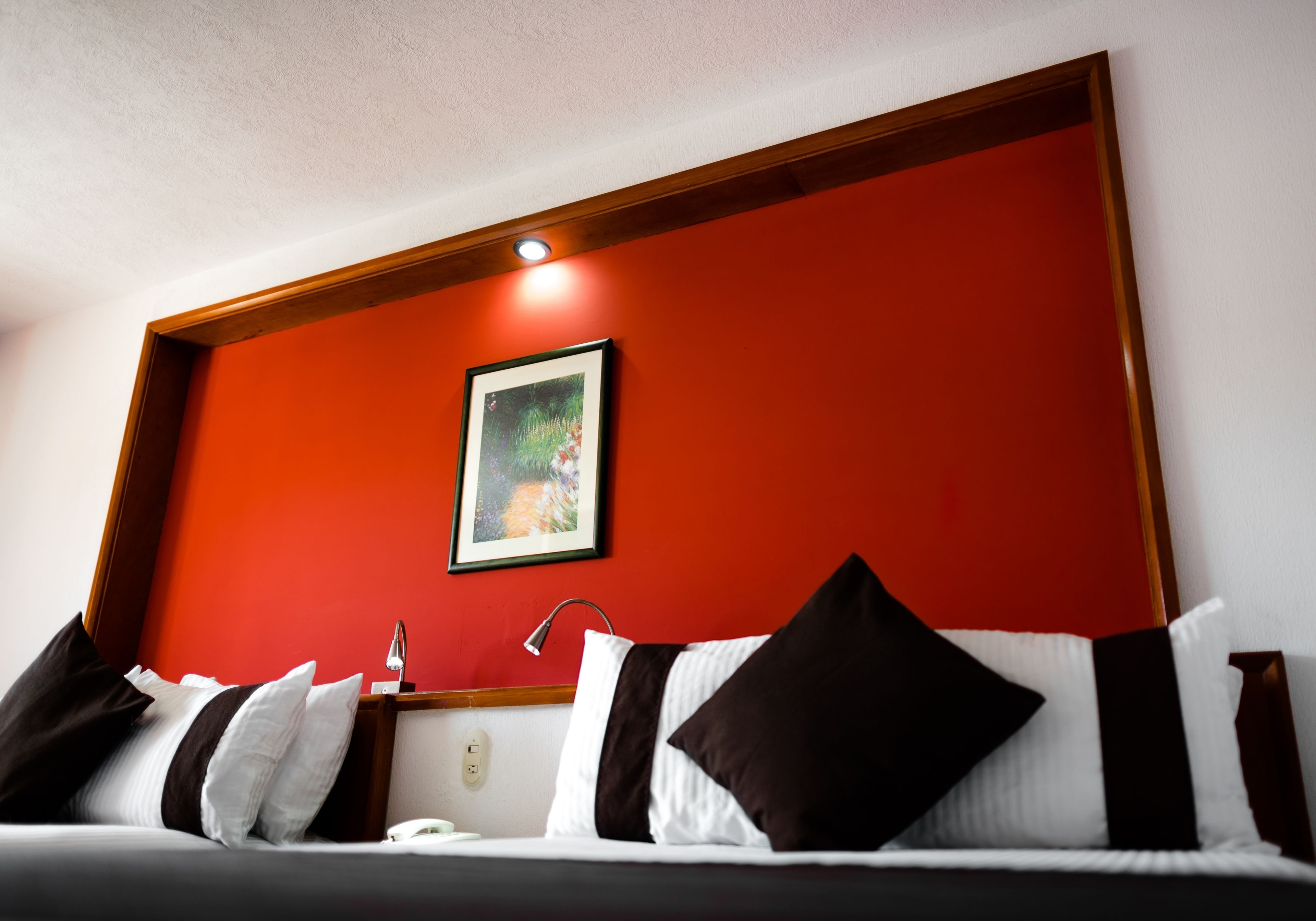 Une chambre d’hôtel avec un mur d’accent rouge, un tableau encadré et un lit avec une literie blanche et noire.