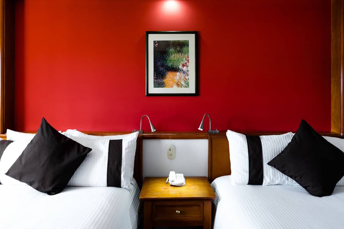 A hotel room with two beds, a wooden nightstand, a telephone, and a painting on the wall.