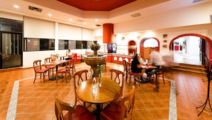 A spacious dining area with wooden tables and chairs, a central fountain, and a large stained glass window above. - Mision Express Celaya (Celaya)