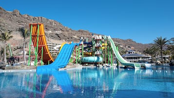 Enjoy thrilling water slides and a refreshing pool surrounded by lush palm trees and rugged hills.