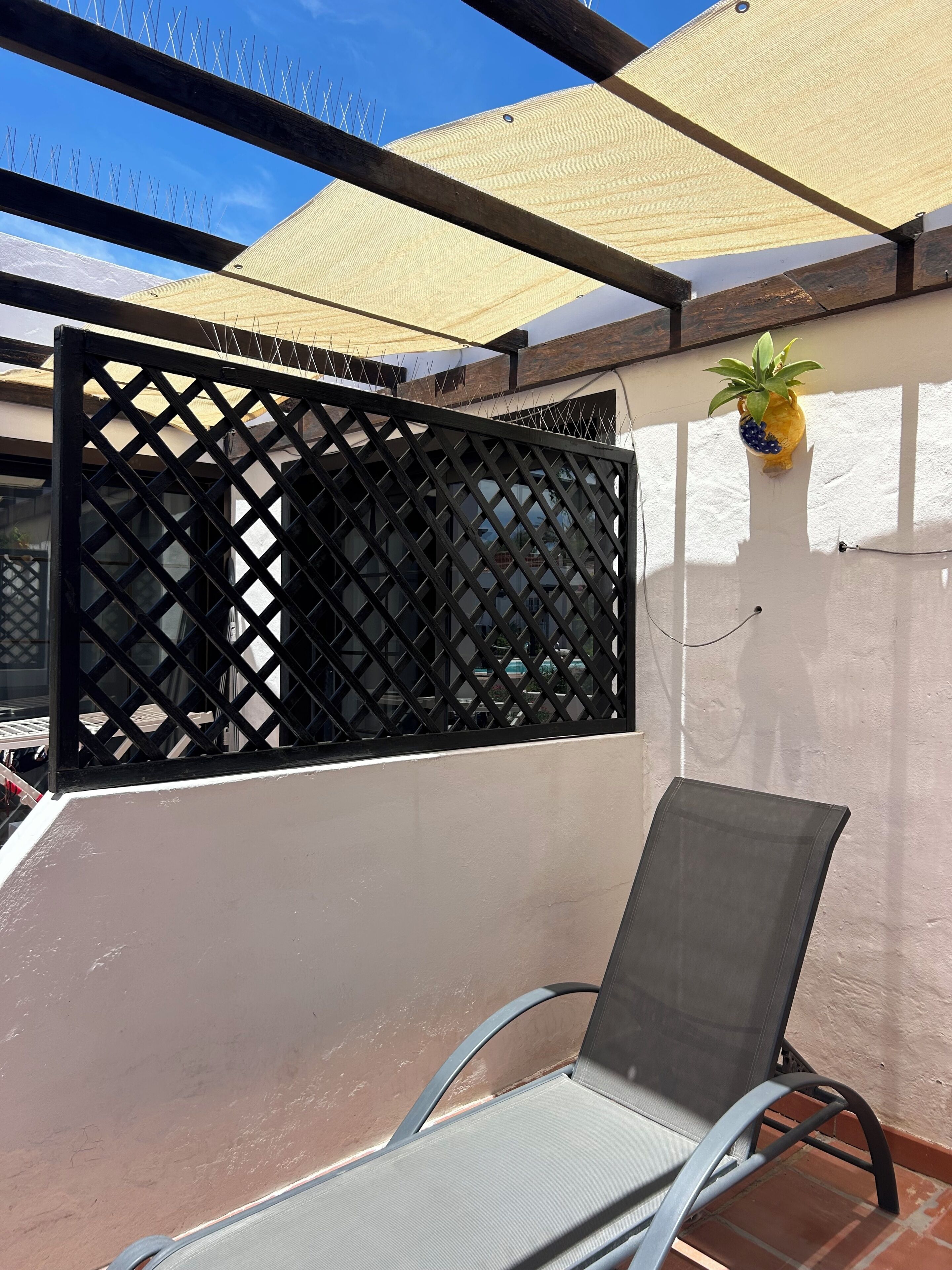 Ein Balkon mit einem Metallstuhl, einer schwarzen Gitterabtrennung und einem Blumentopf.
