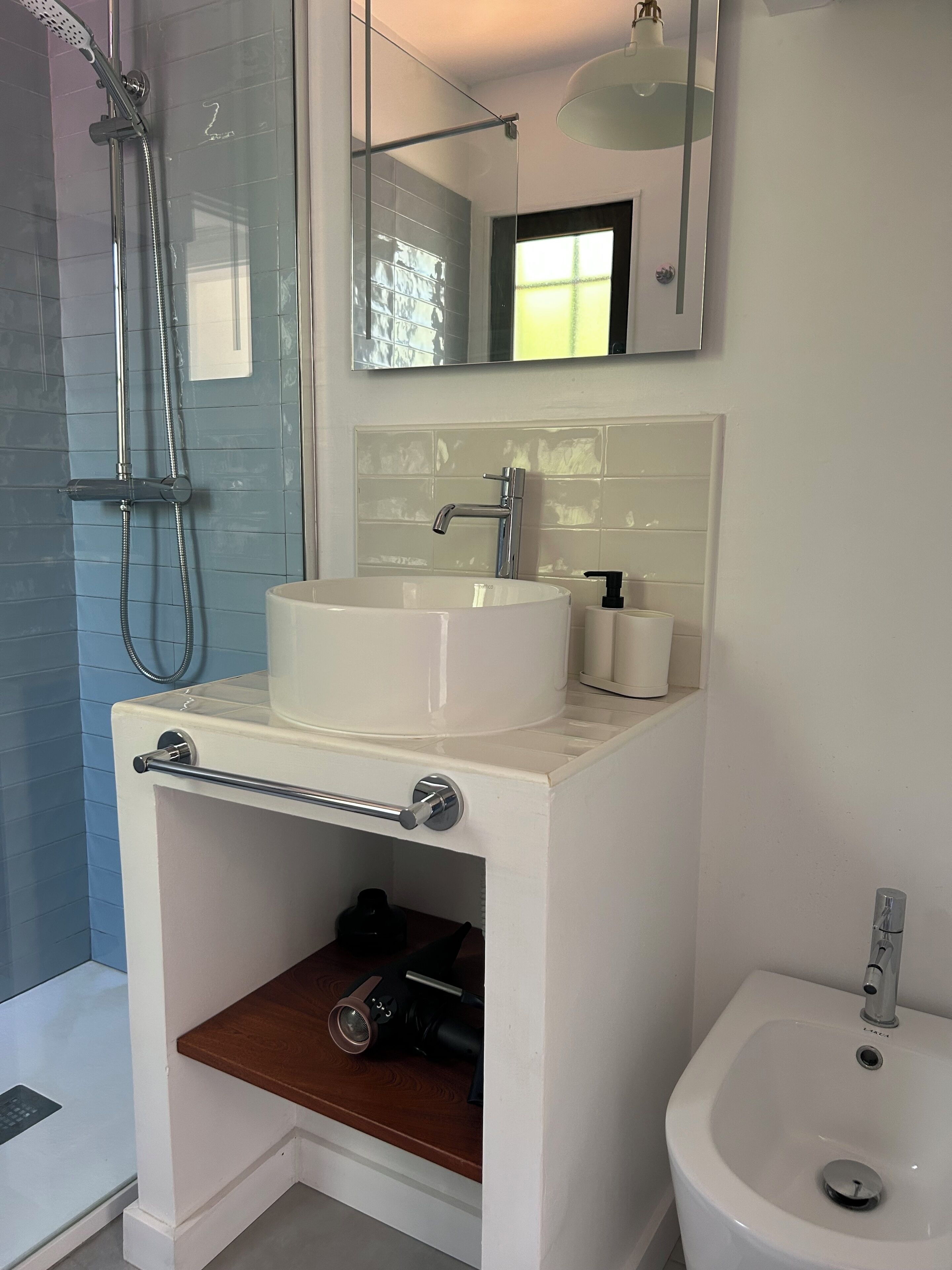 A bathroom with a white sink, a mirror, a handheld showerhead, and a bidet.