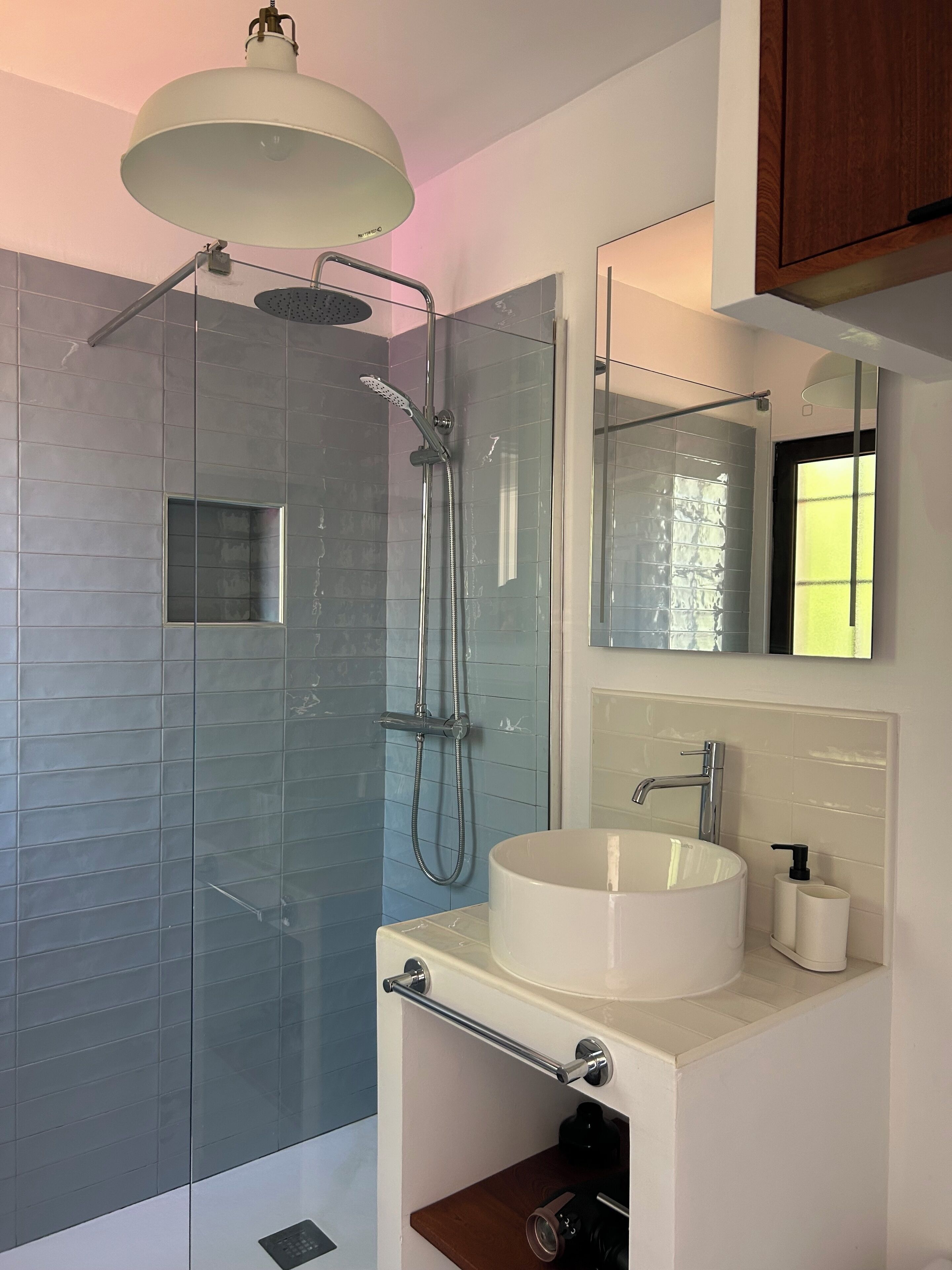 A modern bathroom with a glass-enclosed shower, a white sink, a mirror, and a wooden cabinet.