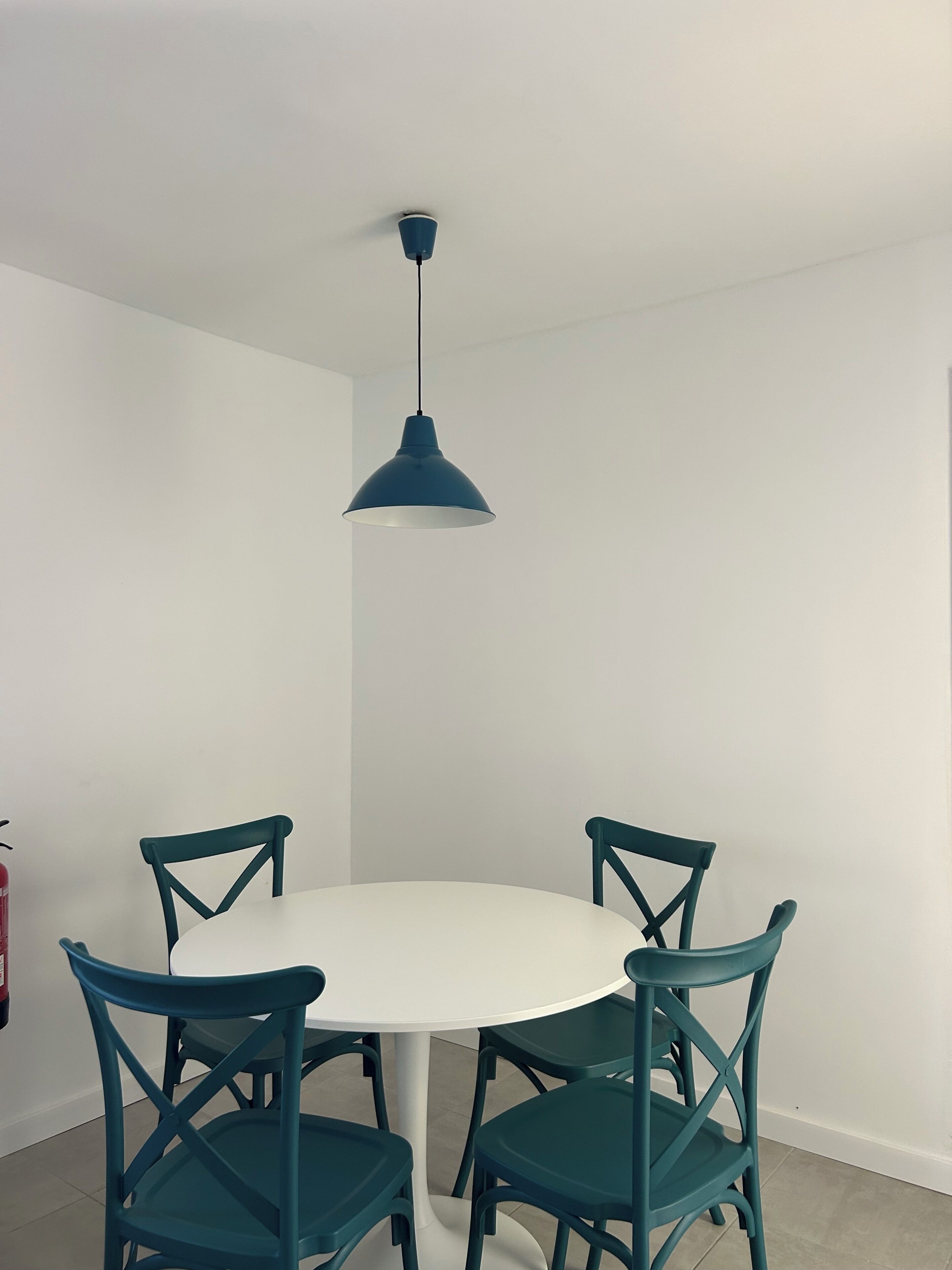 A dining area with a round table and four chairs, a blue pendant light, and white walls.