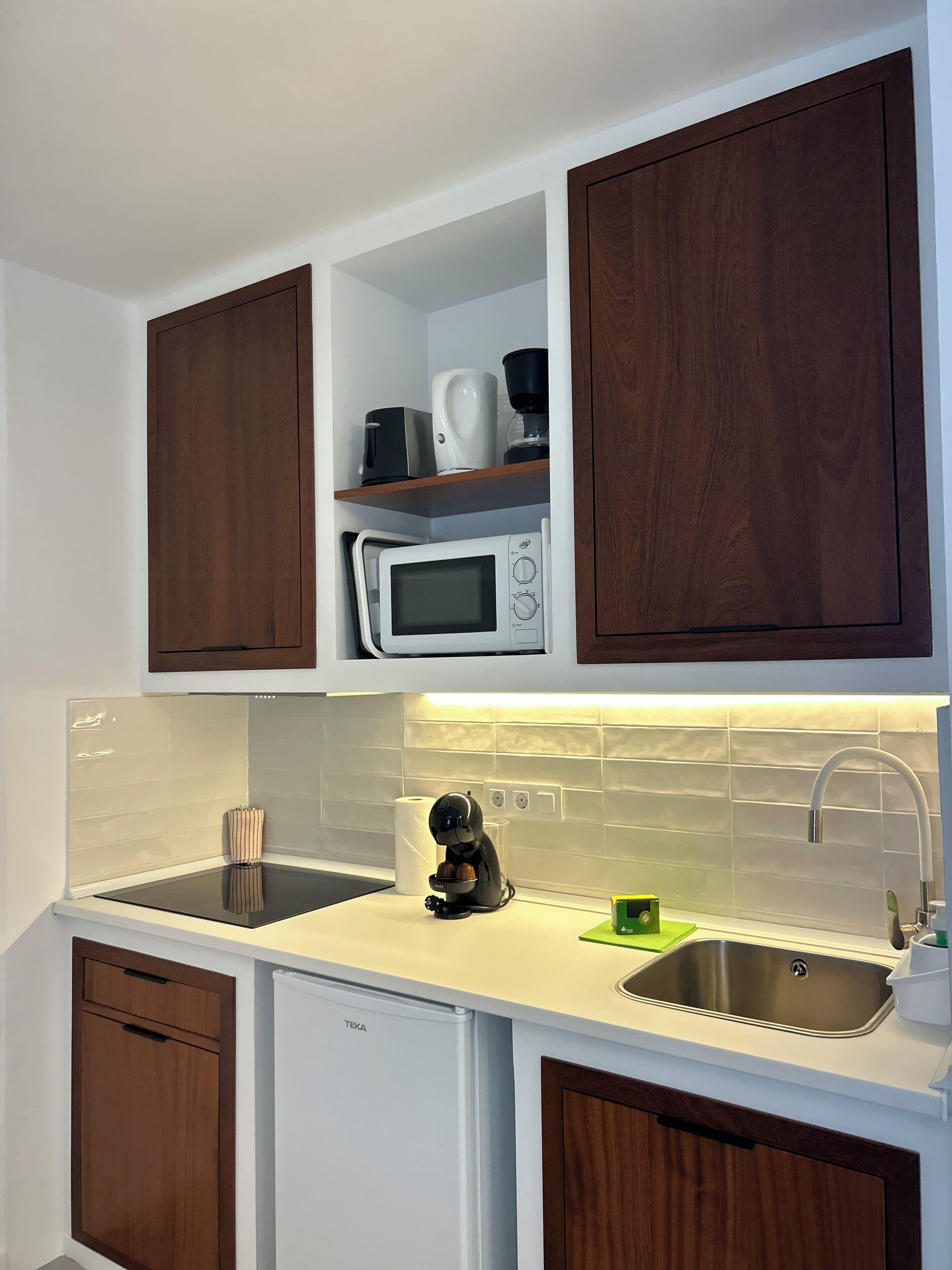 A compact kitchen with wooden cabinets, a microwave, a coffee maker, a sink, and a dishwasher.