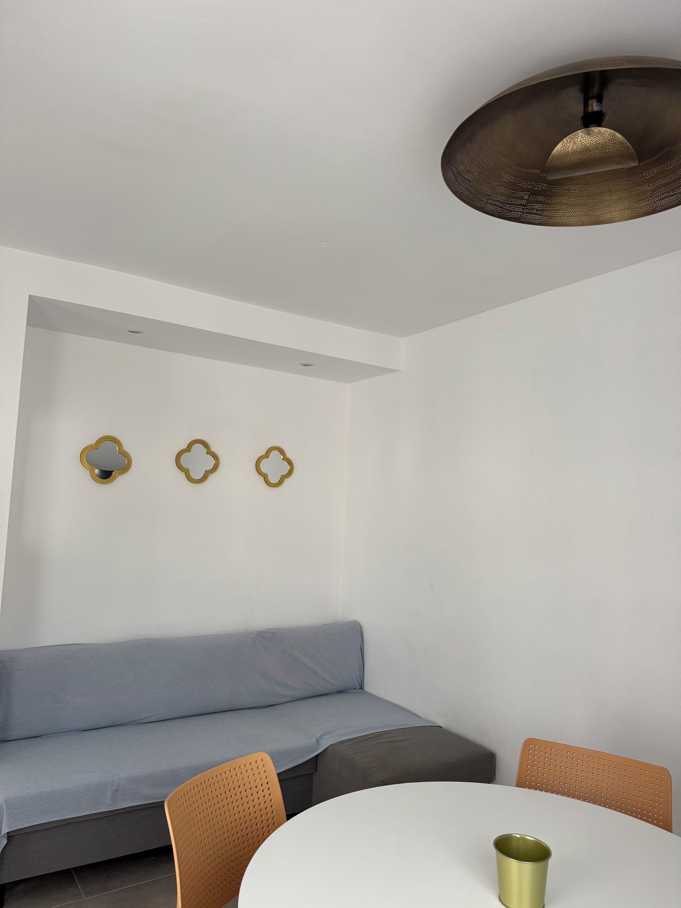 A room with a white ceiling, a round table with a metal cup, a gray sofa, and three wall-mounted decorative items.