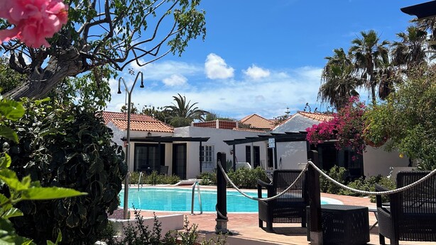 Ein Poolbereich mit Liegestühlen, blauem Himmel und einem Gebäude mit einem Ziegeldach im Hintergrund.
