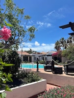 Ein Poolbereich mit Liegestühlen, blauem Himmel und einem Gebäude mit einem Ziegeldach im Hintergrund.