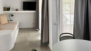 Ein zeitgemäßer Wohnraum mit einem weißen Sofa, einem Esstisch und einer Küchenzeile inklusive Fernseher.