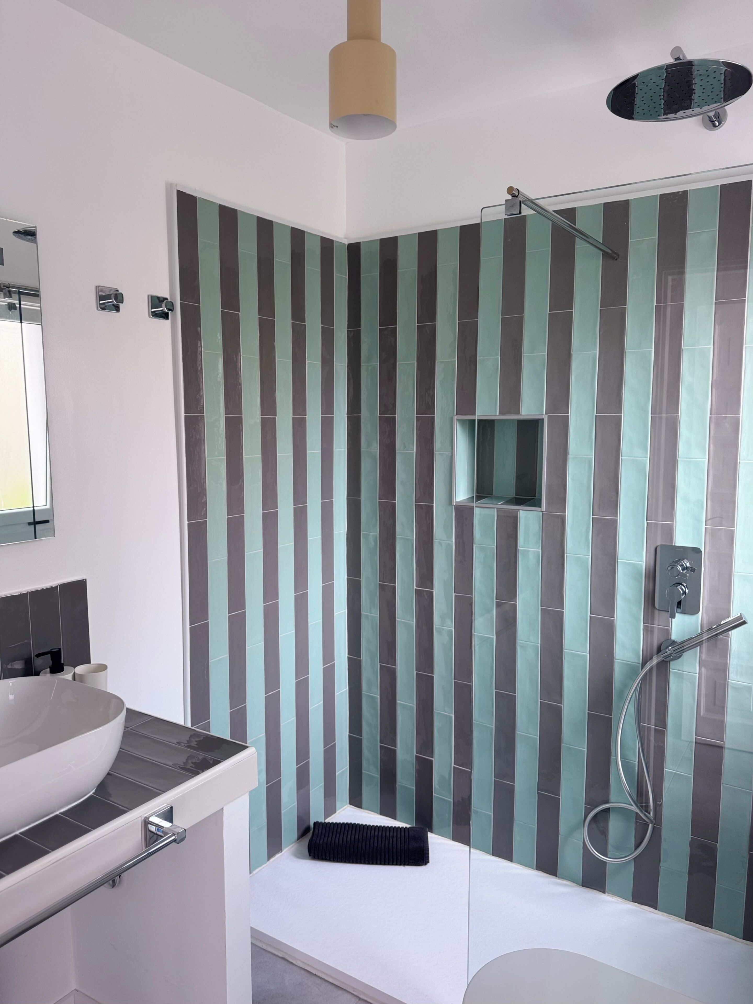 A modern bathroom with a large sink, a shower with a handheld showerhead, and a towel rack.