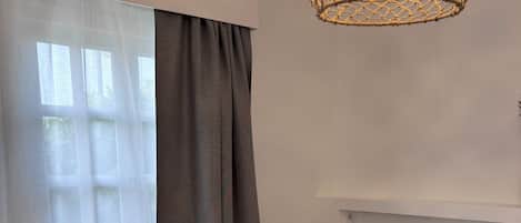 A neatly made bed with rolled towels, a hanging light fixture, and sheer curtains.
