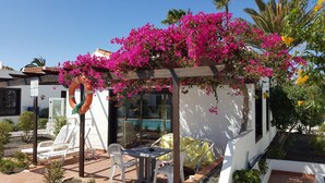 Ein überdachter Außenbereich mit Blick auf einen Pool, weißen Wänden und rosa Bougainvillea-Blumen.