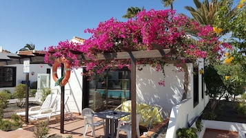 Ein überdachter Außenbereich mit Blick auf einen Pool, weißen Wänden und rosa Bougainvillea-Blumen.