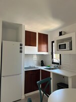 Cocina compacta con armarios blancos, microondas integrado, refrigerador y lavamanos.