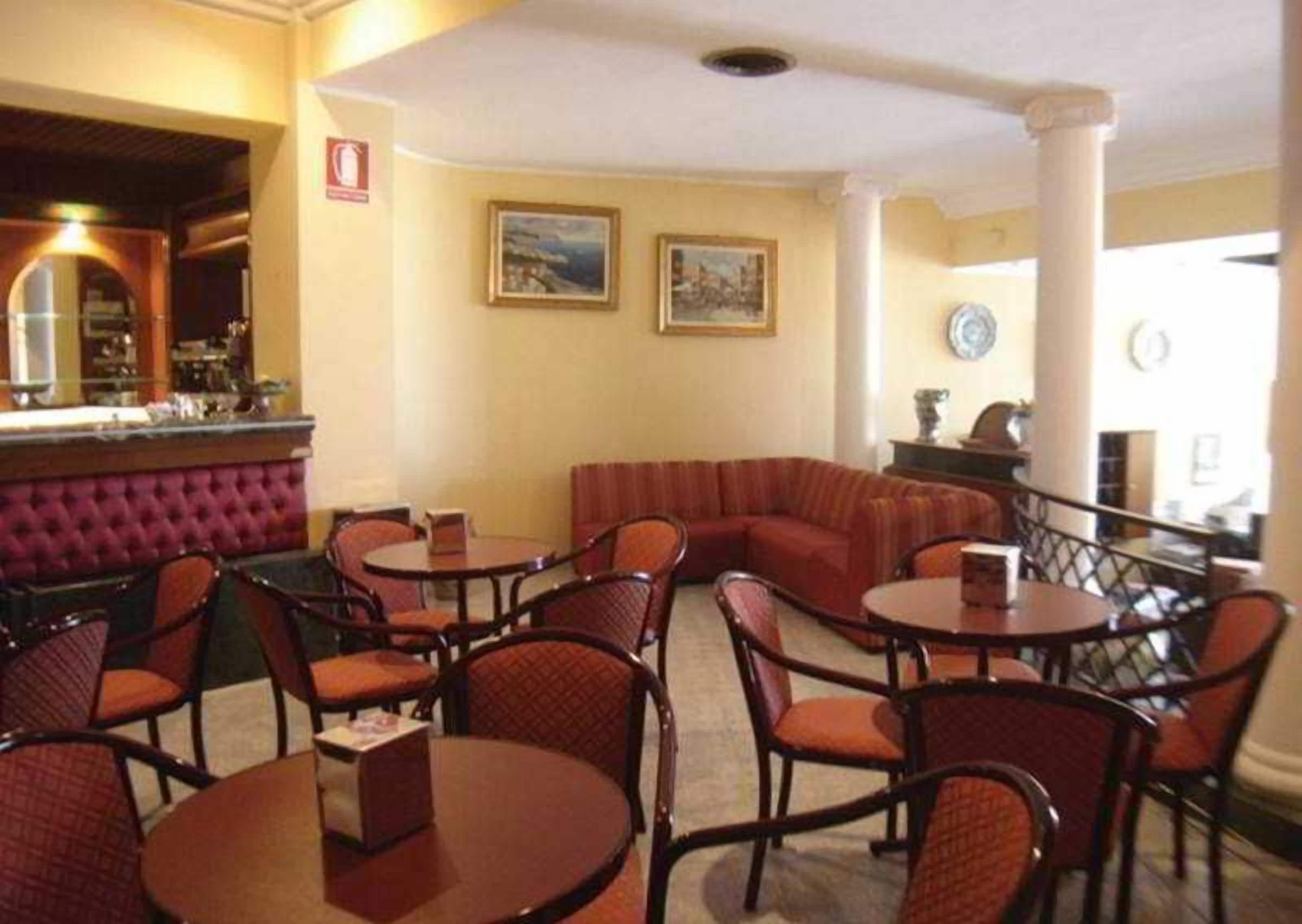 A restaurant with round tables and cushioned seating, a bar area, and framed artwork on the walls.