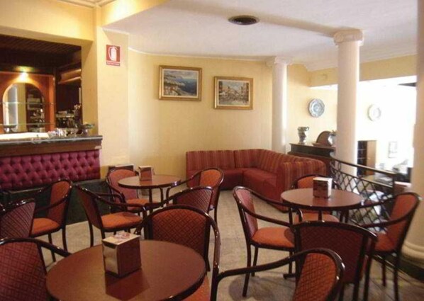 Un restaurant avec des tables rondes et des sièges rembourrés, un coin bar et des œuvres d’art encadrées qui ornent les murs.