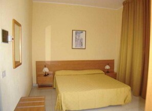 Quarto de hotel com uma cama de solteiro, mesas de cabeceira, um quadro na parede e uma cortina na janela.