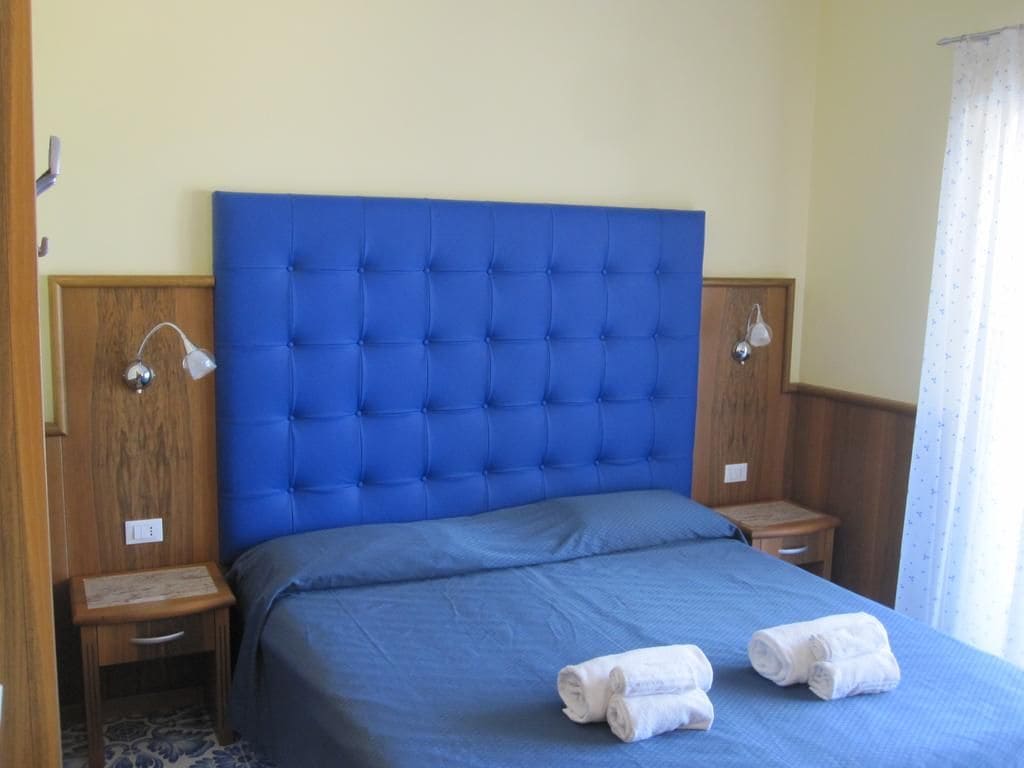 A hotel room with a large bed, two bedside tables, and a window with curtains.