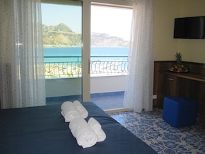 Une chambre d’hôtel avec un lit, un bureau, une télévision et une vue sur la mer.